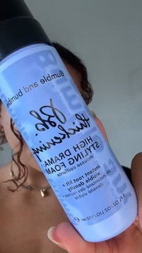 Person hält Blase und Flasche mit hochdramatischem Styling-Schaum mit schwarzem Deckel und blauem Etikett nahe an der Kamera.