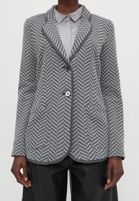 Blazer gris de espiga con cuello con muescas, dos bolsillos delanteros, dos botones y ribete contrastante a lo largo de los bordes. Fabricado en tela texturizada.