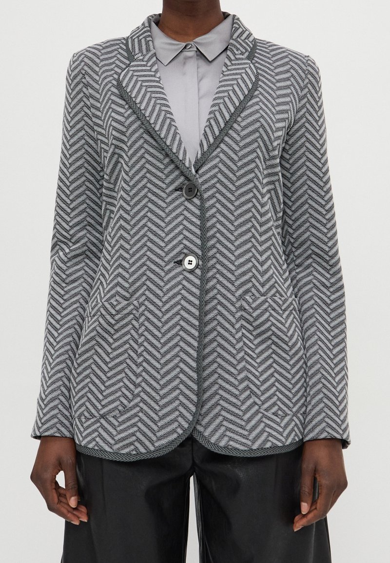 Blazer gris de espiga con cuello con muescas, dos bolsillos delanteros, dos botones y ribete contrastante a lo largo de los bordes. Fabricado en tela texturizada.