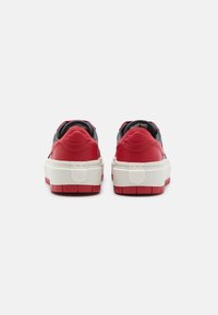 Une paire de baskets rouges basses avec des semelles blanches épaisses, vue de l'arrière sur un fond blanc.