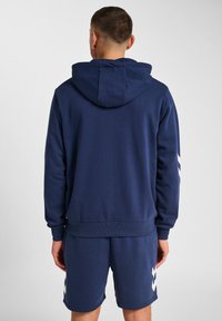 Haut à capuche bleu marine avec une capuche arrière, un ourlet en côtes et des accents en chevron blancs sur les manches. Assorti avec un short bleu marine, le tout en tissu doux.