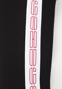 Leggings neri con una striscia bianca lungo il lato, decorati con un logo rosso in un motivo ripetuto. Tessuto liscio e elasticizzato.