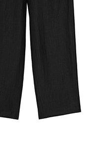 Pantaloni neri in lino larghi e fluidi mostrati distesi, che mettono in evidenza il tessuto strutturato e il design semplice e rilassato.