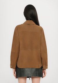 Giacca in finta suede marrone con colletto, maniche lunghe e polsini abbottonati, caratterizzata da un orlo dritto e dettagli di cucitura minimi.