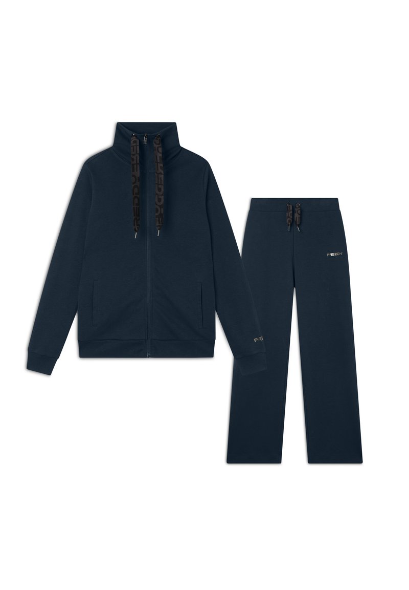 Completo tuta blu navy composto da giacca con zip e pantaloni abbinati, caratterizzato da un colletto alto, tasche laterali e dettagli con logo.