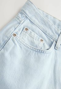 Tissu en denim bleu clair, présentant une poche arrière avec des accessoires en argent. Texture douce avec de subtiles lignes diagonales et des détails de couture.
