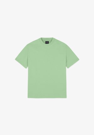 Jasnozielona bawełniana koszulka z okrągłym dekoltem, krótkimi rękawami i luźnym krojem, w połączeniu z niebieskimi dżinsami. Bez wzorów ani akcentów.