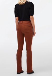 Jean évasé marron avec poches, doté d'une taille ajustée et d'une texture douce. Stylisé avec un haut noir à manches courtes et des chaussures noires.