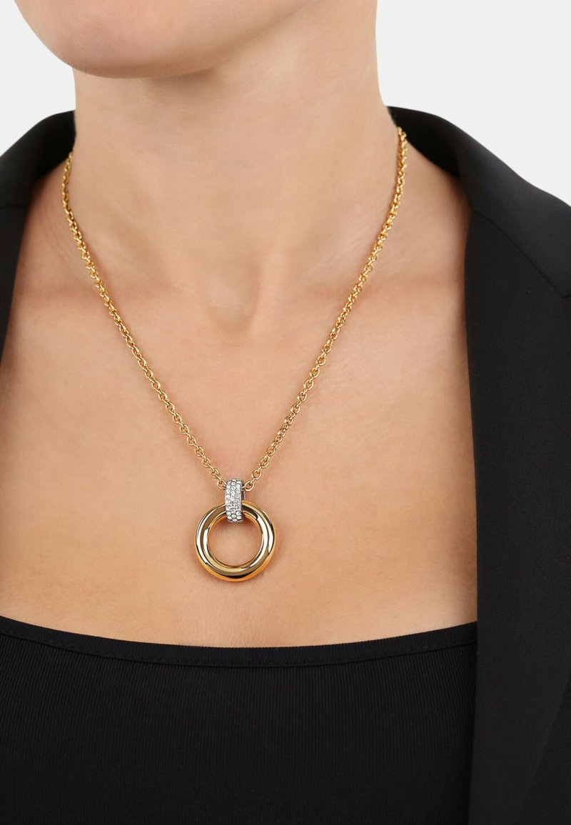Collana in metallo dorato che presenta due anelli intrecciati e un'accento di strass, appesa a una catena delicata.