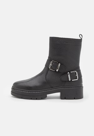 Bottine en cuir noir à finition texturée, avec deux boucles argentées, une semelle robuste et une languette de tirage pour un enfilage facile.