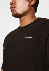 Sort bomulds t-shirt med rund hals og korte ærmer, prydet med en hvid "Calvin Klein" logo broderet på brystet.