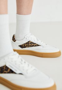 Baskets blanches avec un panneau latéral en imprimé léopard, upper en cuir texturé et semelle en gomme. Assorties à des chaussettes blanches côtelées.