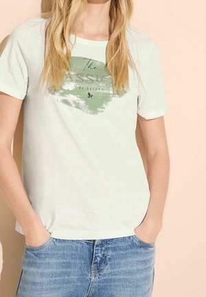 Jasnozielona bawełniana koszulka z okrągłym dekoltem, krótkimi rękawami i nadrukiem z tekstem oraz dekoracjami w formie liści. Noszona z dżinsowymi szortami.