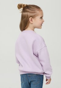Felpa viola con spalle scese e polsini a coste, abbinata a jeans blu. Tessuto morbido, design casual, presenta un collo rotondo.