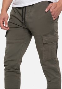 Olijfgroene cargobroek met elastische tailleband, trekkoord, meerdere zakken en stikdetails, gemaakt van duurzaam materiaal.