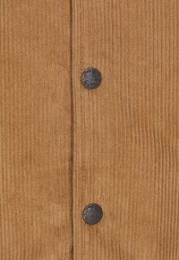 Bruine corduroy blouse met verticale ribbels, twee metalen knopen en een klein logo detail op de bovenste knop.