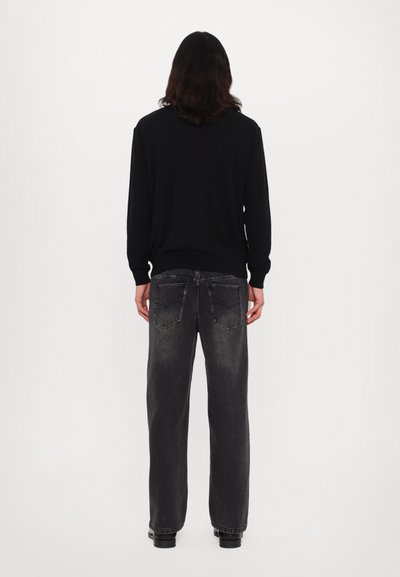 Un pull noir à manches longues associé à un jean noir délavé et ample. Les détails notables comprennent des poches arrière doubles et une texture subtile sur le tissu.