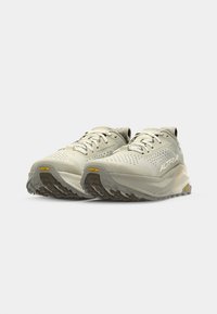 Světlé béžové sportovní boty s texturovaným svrškem, výraznou šněrovací soupravou a podešví Vibram. Mají polstrovanou podrážku a elegantní, moderní design.