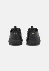 Sneakers sportivi neri con tomaia testurizzata, materiali a contrasto, dettagli dorati e una suola spessa con il logo PUMA.