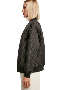 Gepolsterte schwarze Bomberjacke mit gerippten Bündchen und Saum, ausgestattet mit einem Reißverschluss und einem Rautenmuster auf glattem Material.