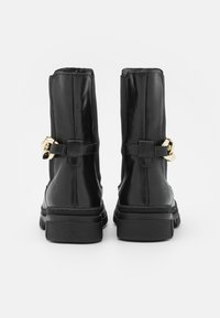 Botas de cuero negras hasta el tobillo con una textura suave, que presentan una hebilla dorada como acento y una gruesa suela de goma negra para mayor estabilidad.