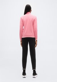 Ροζ φούτερ με ψηλό γιακά και λευκό περιθώριο, συνδυασμένο με μαύρο παντελόνι. Λείο ύφασμα, άνετη εφαρμογή και αθλητικά παπούτσια.