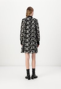 Vestido preto com intricado padrão paisley branco, mangas longas, punhos abotoados e saia ampla. Usado com botas de cano curto pretas de salto.