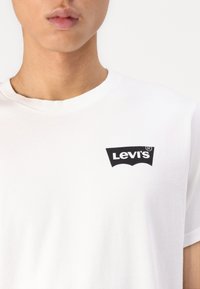 Tricou alb din bumbac cu un logo negru Levi's pe partea stângă a pieptului. Mâneci scurte și design cu gât rotund. Textură netedă.