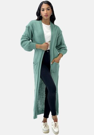 Cardigan lungo aperto in morbido knit verde menta con rifiniture a coste e due tasche frontali, abbinato a una maglia bianca e leggings scuri.