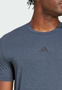 Camiseta deportiva azul hecha de una tela suave y texturizada, con cuello redondo y mangas cortas, y un logotipo negro de adidas en el pecho.