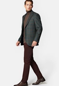 Zielony marynarkowy żakiet w kratę z brązowymi akcentami, noszony na dopasowanym brązowym golfie, w połączeniu z ciemnobrązowymi spodniami i brązowymi butami formalnymi.
