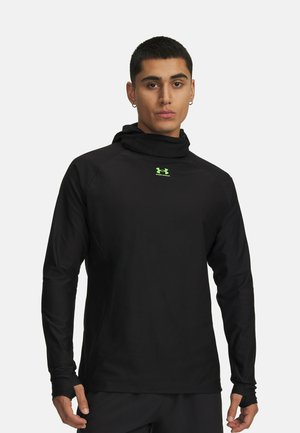 Man wearing black long-sleeve sports hoodie with a neon green Under Armour logo, standing against a plain light background.