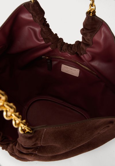 Sac à main en daim marron avec poignées en chaîne dorée, intérieur en cuir bordeaux, poche zippée et étiquette de marque Coccinelle à l'intérieur.