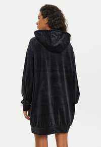 Abito felpa nero con cappuccio, dalla texture morbida e vellutata, maniche lunghe e vestibilità larga, con orlo arricciato in fondo.