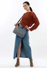 Borsa a tracolla grigia con motivo e zip gialla, tenuta da un modello che indossa un maglione di lana color ruggine e una gonna di jeans, mostrando un dettaglio con spacco.