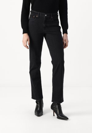 Femme portant un jean noir droit, un haut à manches longues côtelé noir et des bottines noires à talons avec bouts pointus.