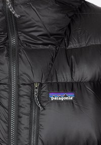 Juodas insulated pūkinis švarkas su nuimamu kapišonu, turintis užtrauktuko priekinę dalį, dvi užtrauktukines kišenes ir "Patagonia" logotipą krūtinėje.
