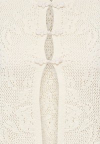 Tissu en dentelle crème avec motifs floraux et trois fermoirs boutons spirales blancs décoratifs le long de l'ouverture centrale.