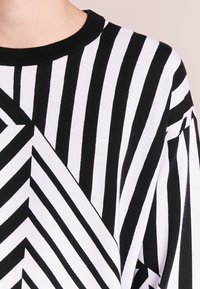Schwarz-weiß gestreifter Pullover mit Rundhalsausschnitt. Hat ein geometrisches Muster aus abwechselnden diagonalen und vertikalen Streifen. Weiche Textur.