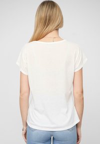 T-shirt blanc à manches courtes avec une coupe décontractée et un col rond, fabriqué en tissu léger, présentant une texture légèrement translucide.