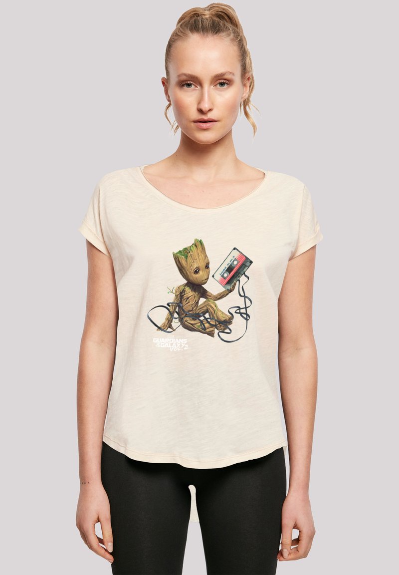Cream-colored short-sleeve t-shirt featuring an illustration of a character with a green plant-like head holding a cassette tape and tangled wires.