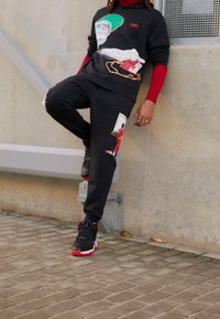 Felpa nera con stampe grafiche colorate e maniche lunghe, abbinata a pantaloni jogger neri con accenti simili e sneakers nere.