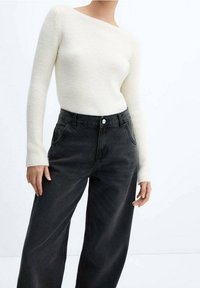 Kermainen ribbineulottu pitkähihainen yläosa olkapäät paljastavalla designilla, yhdistetty korkeavyötäröisiin mustiin leveälahkeisiin farkkuihin, joissa on sivutaskut ja etunappi.