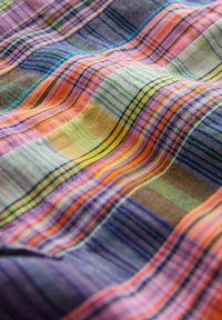 Farverigt vævet stof med vandrette og lodrette striber i pink, orange, gul, grøn, blå og lilla, der viser tekstur og folder.