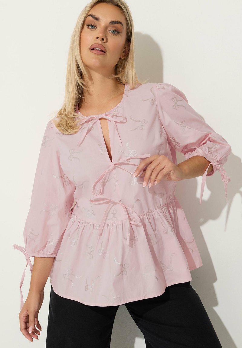 Blusa rosa realizzata in un tessuto leggero, con fiocchi argentati ricamati su tutta la superficie, con nodo al collo e vita e maniche arricciate.