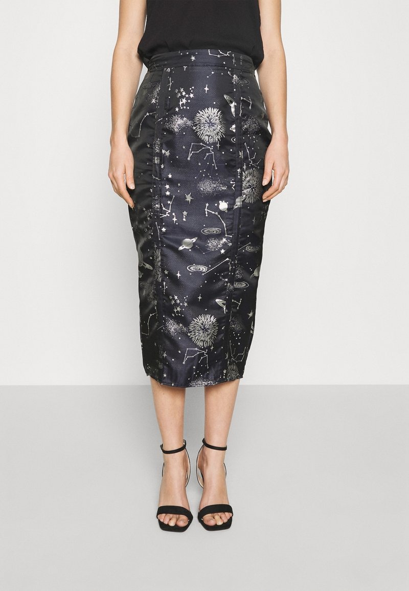 Femme portant une jupe crayon noire taille haute avec des motifs blancs sur le thème de l’espace et des talons noirs ouverts avec bride à la cheville, sur fond blanc.