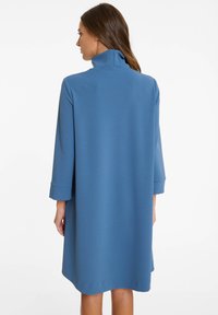 Blaues, übergroßes Kleid mit hohem Kragen, drei Viertelärmeln und glattem Stoff. Das Kleid hat ein lockeres, fließendes Design, das knapp über dem Knie endet.