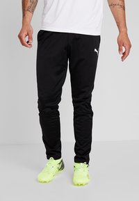 Sorte atletiske bukser lavet af letvægtsstof med en tætsiddende pasform. Har et hvidt Puma-logo på venstre hofte og elastiske stropper ved anklerne.