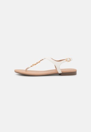 Witte platte sandaal met een T-band ontwerp, gouden kettingaccent en beige zool. Verstelbare enkelband voor een veilige pasvorm. Glad leren textuur.