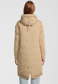 Lang beige polstret frakke med hætte, der har bånd og knapdetaljer ved kanten og ærmerne. Glat tekstur med et minimalistisk design.